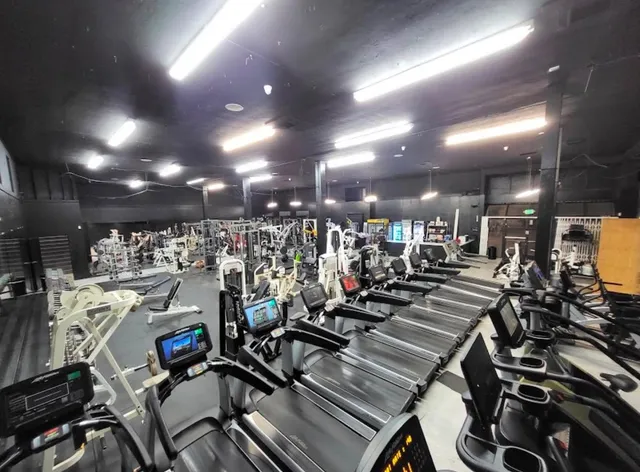 Same space finished and equipped as a gym, with rows of treadmills and strength equipment