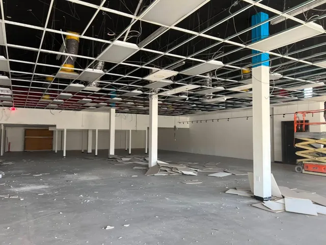 Gutted commercial space with exposed ceiling grid, bare concrete floor, and construction debris