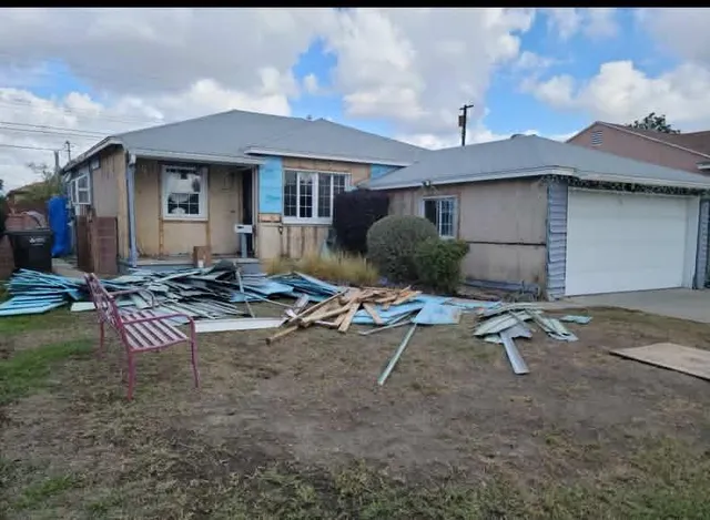 Home exterior mid-remodel with old siding stripped down to the sheathing and a debris pile in the yard