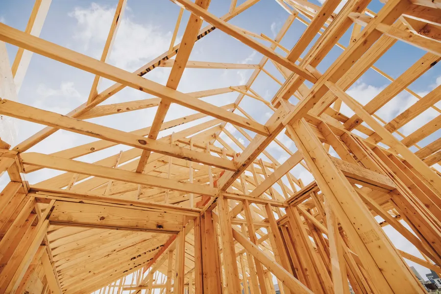 View looking up through open wood roof framing against a blue sky